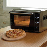 A freshly baked Neapolitan pizza topped with prosciutto ham resting on a wooden serving board in front of an Effeuno P134HA 509 °C Pro electric pizza oven with an illuminated baking chamber - La Pizza Hub